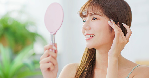 skin care concept - close up of asian confident woman is smiling and looking her good skin in mirror