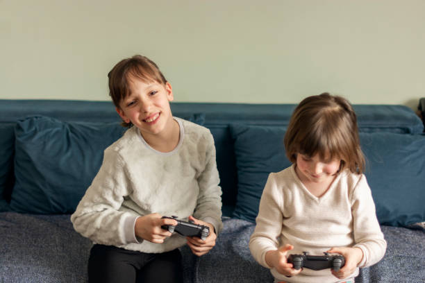 istock Two happy girls sitting on sofa and playing video game 1702143311
