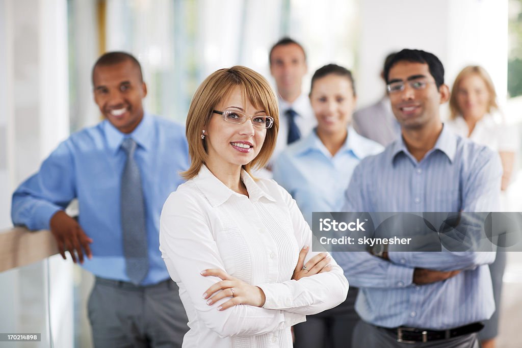 Businesswoman in white with colleagues in blue Successful businesspeople looking at the camera. The focus is on the Caucasian woman.   Organized Group Stock Photo