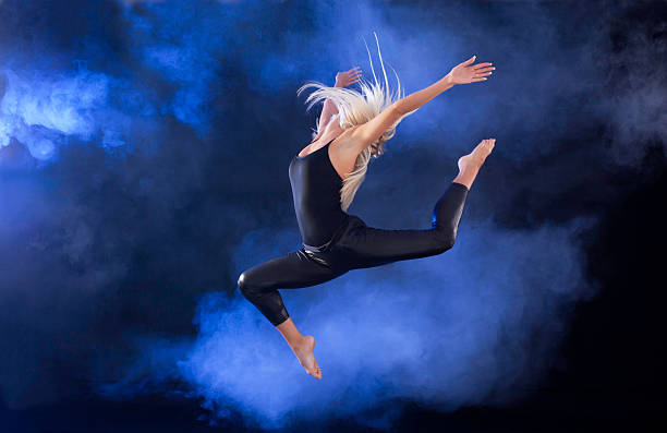Professional ballerina jumping through the fog. Young professional ballet dancer jumping through the black and blue fog.    jazz dancing stock pictures, royalty-free photos & images