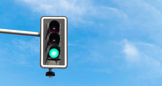 Traffic light on green, with blue sky and clouds on the background. Copy space