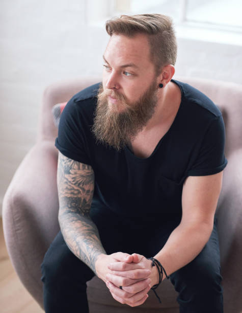 istock Young hipster man with beard sitting looking out window contemplating 1702176139