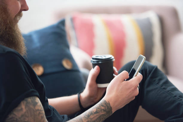 istock hipster man using smartphone browsing messages on social media texting on mobile phone holding coffee 1702176145