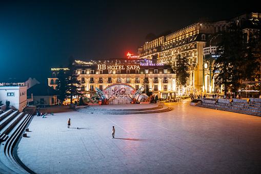 Sa pa, Vietnam - November 13, 2022: few people walking on huge illuminated town square with hotels in Sa pa at night