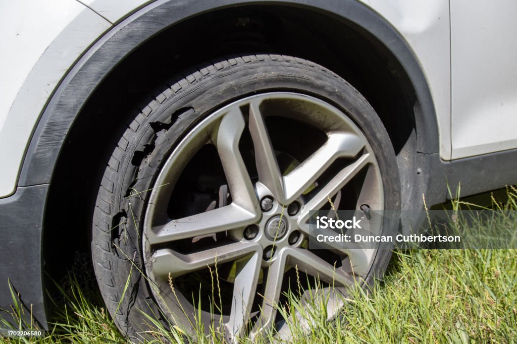 A car with a flat tyre after a large blow out on the highway showing a large slit in the tyre at the side of the M25 motorway in London in the UK Accidents and Disasters Stock Photo