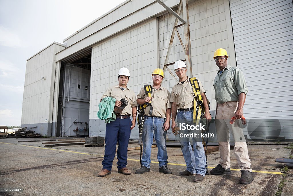 Team of construction workers with harnesses Multi-ethnic construction workers (20s and 30s) with hard hats, safety glasses and harnesses. Group Of People Stock Photo