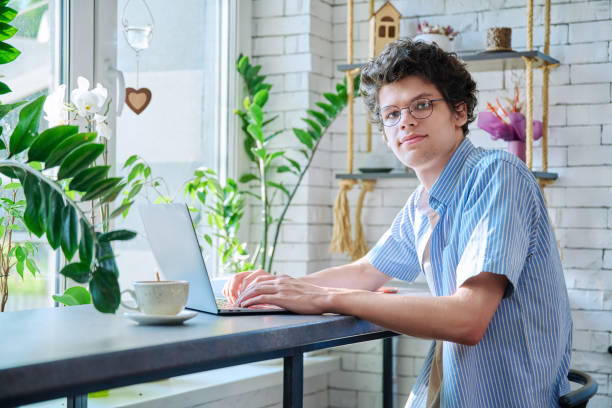 istock Young guy is university student typing on laptop, sitting in coffee shop at table with cup of coffee 1702226055