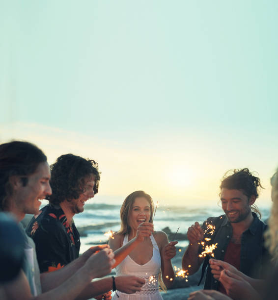 friends with sparklers celebrating new years eve on beach at sunset - independence lifestyles smiling years imagens e fotografias de stock