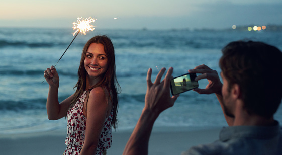 Beautiful woman holding sparkler posing for photo on romantic beach celebrating new years eve at sunset