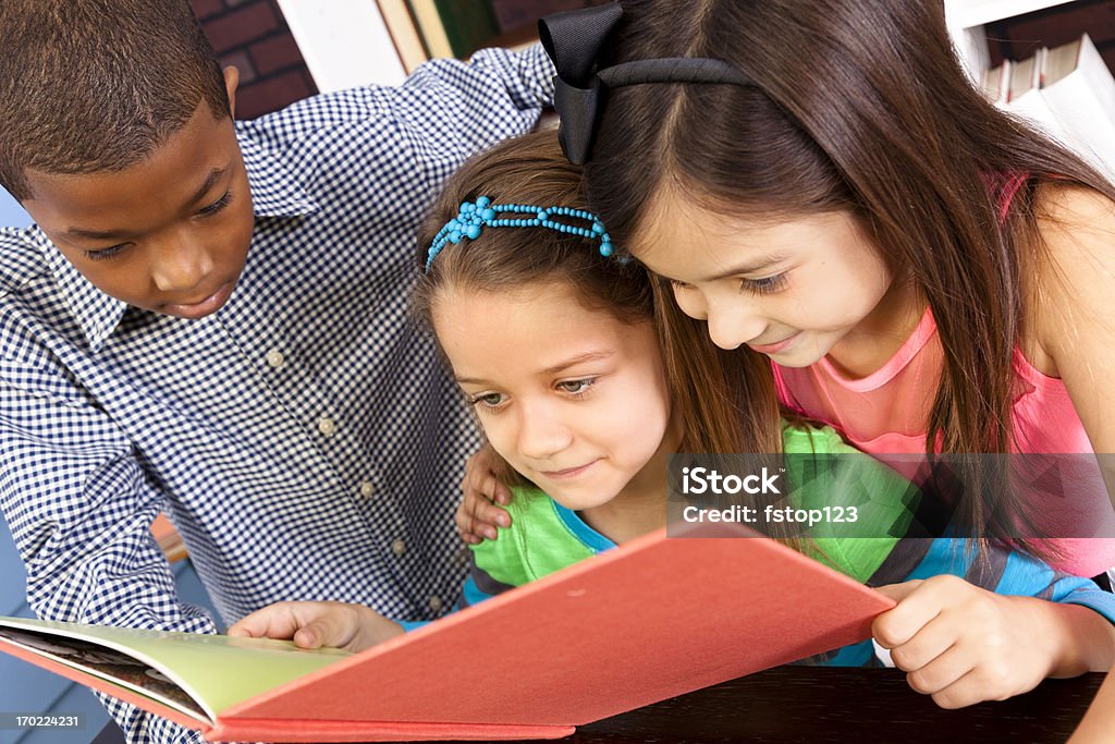 Multi-etnico elementare 7-8 anni cercando di libro a scuola Libreria - Foto stock royalty-free di 6-7 anni