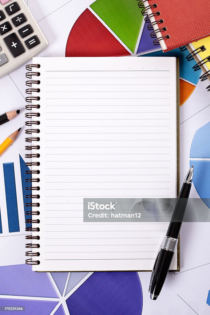 Financial background with blank notepad Blank lined paper notebook with ballpoint pen surrounded by various charts and graphs, pencils, books and calculator.  Space for copy.   Alternative version shown below:  Color Image Stock Photo