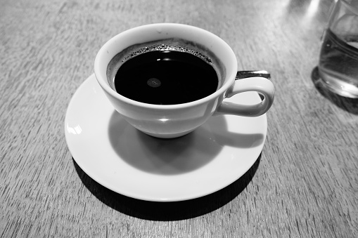 Beauty coffeecup standing on wooden table with dark tasty coffee, brown old table consisting of liquid coffee in coffeecup, golden spoon, small plate, porcelain coffeecup for coffee at antique table