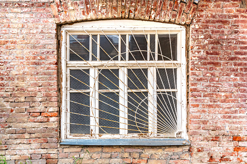 Old window with bars on brick weathered wall of a rural house