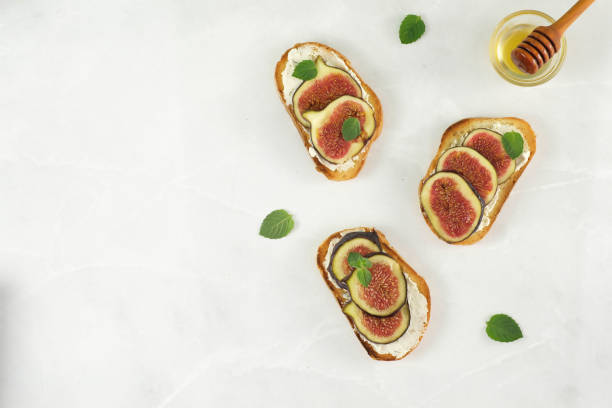 istock Bruscetta with figs, cheese and honey on a marble background. Top view. 1702283268
