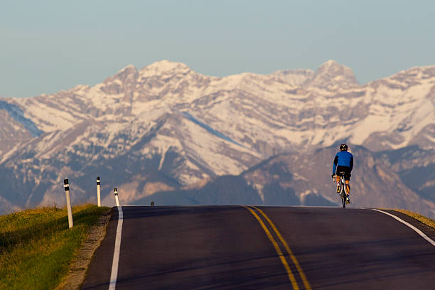 A male road bicyclist rides west towards the Rocky Mountains in Alberta, Canada.