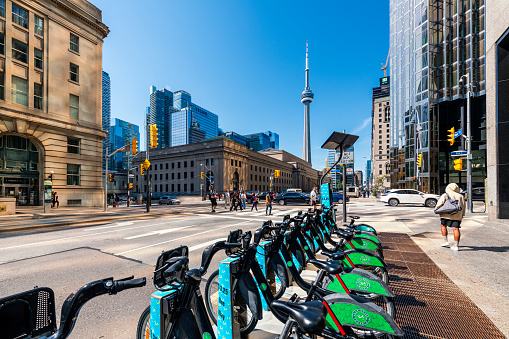 Toronto, Canada - September 2, 2022: Some skyscraper and the CN tower at Toronto downtown. Many bikes in a row at a bike rental station in front.
