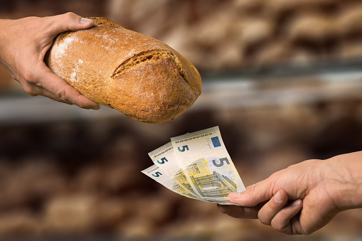 Inflation concept: paying 15 euros for one loaf of bread. Closeup of the hands of the buyer and the seller in front of the bread counter