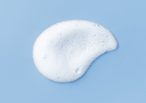 White skincare cleansing foam on light blue background. Soap, shampoo or shower gel foam texture, close-up, top view