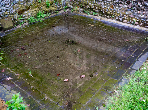 A blocked drain in a corner of the churchyard directly outside St Peter & St Paul’s church in Lavenham, Suffolk, Eastern England, which has caused a bit of a flood.