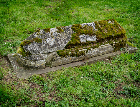 A very old ledger tomb partially covered in moss in the churchyard of St Peter and St Paul's Church in Lavenham, Suffolk, Eastern England. It appears to show a mason’s mark on the top. The church was constructed 1486-1525 in what was then one of the largest and richest towns in England.