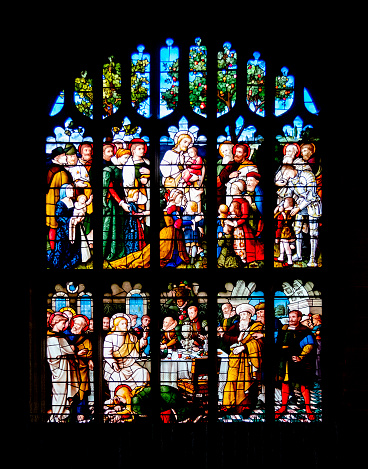 A brightly-coloured stained glass window in St Peter and St Paul's Church in Lavenham, Suffolk, Eastern England. The window depicts,”Jesus said, Suffer little children, and forbid them not, to come unto me: for of such is the kingdom of heaven.