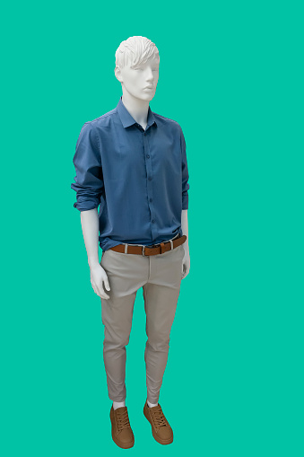 Full length image of a male display mannequin wearing blue long-sleeved button up shirt and gray trousers isolated on green background