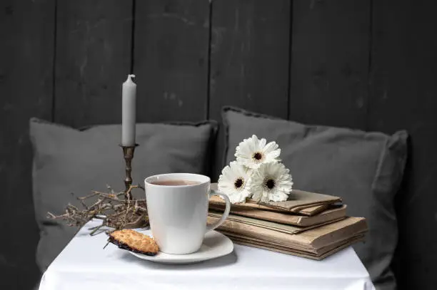 On the coffee table are attributes for a relaxed break: coffee with a cookie, some flowers on old books and a candle