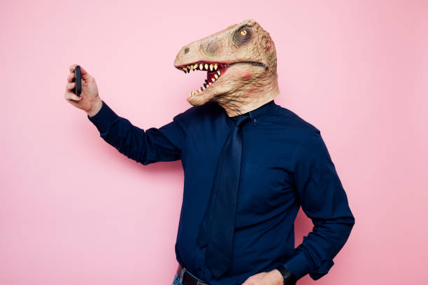 istock Man with dinosaur mask taking a selfie with smartphone 1702355680