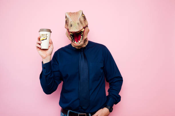 istock Man with dinosaur head holding a cup of coffee 1702356979