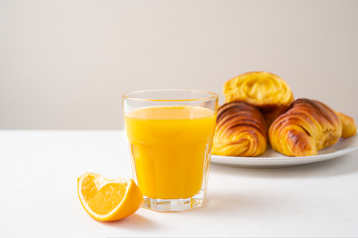 Portuguese Brioche croissants with orange juice in glass. Beige and orange colours