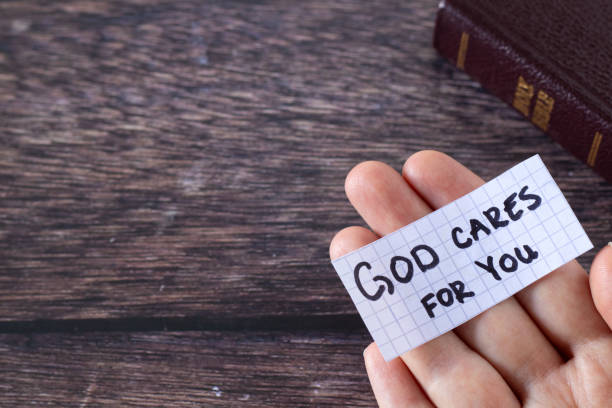 god cares for you, handwritten text note on human hand and holy bible book on wooden table - jesus christ human hand god consoling imagens e fotografias de stock