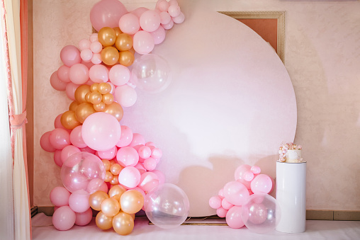 Arch decorated with pink, white and golden balloons. Trendy baptism cake for girl. Delicious reception at a birthday party. Photo wall decoration space or place for text. Celebration concept.