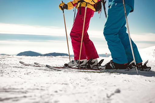 Close-up photo of legs. Two skiers male and female stands with ski poles