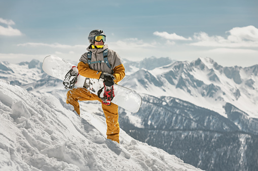 Handsome male snowboarder stands at ski slope with snowboard in hands. Ski resort concept