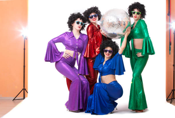 un grupo de chicas con trajes coloridos con una bola de discoteca posan en el estudio sobre un fondo blanco. - disco ball 1970s style 1980s style nightclub fotografías e imágenes de stock