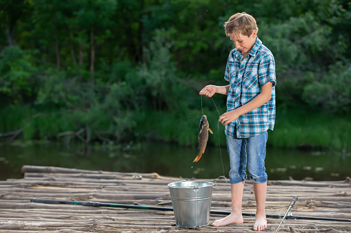 A fisherman boy stands on a wooden bridge and looks at the caught carp.