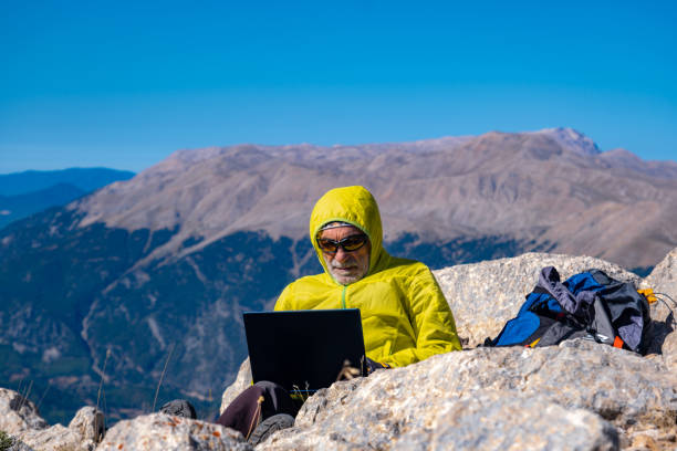 istock 60-65 year old man with a backpack using a laptop at the top of the mountain. 1702426126