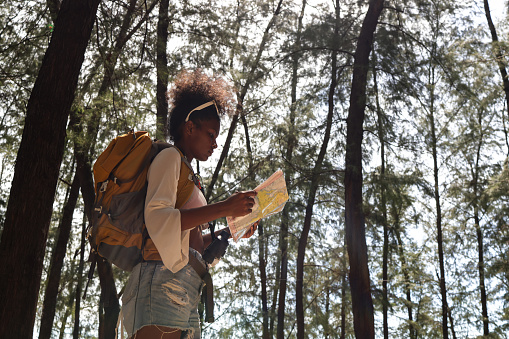 The black woman  with a backpack trekking in the woods and holding the map