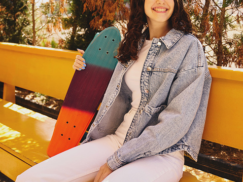 Girl sitting at the bench, her skate board by her