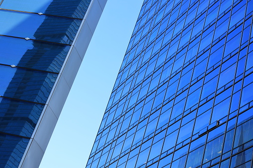 Low angle shot of the facade of a commercial building with blue windows under blue sky. Illustration of commercial and business district (CBD)