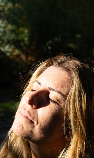 Caucasian blonde mature adult woman in the morning enjoying the sun relaxing and breathing deep. concept of charging energy and positivity.vertical image.