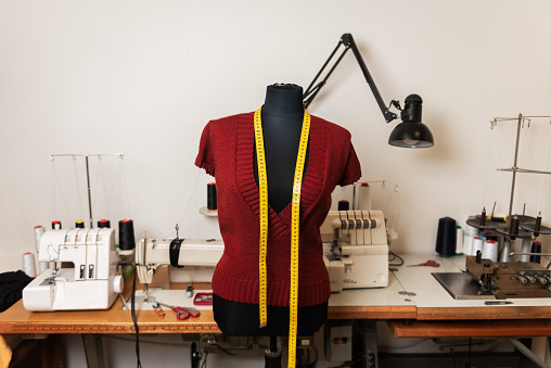 Tailors dummy with a sweater and a measuring tape on it. Sewing workshop, tailors workshop in the background with sewing machines and sewing tools