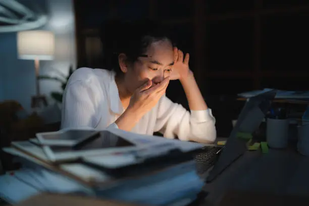 Late-night freelancer, Dedicated Asian woman working overtime on laptop computer, meeting deadlines in the sleepy Night, Businesswoman burning the midnight to working hard, sleep at working desk
