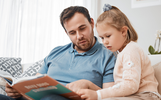 Bonding, reading and father and child with a book on the sofa for learning or knowledge. Relax, family and a man, dad or girl kid with a story for education or teaching together in a home living room