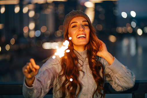 Portrait of a young woman holding a burning sparkle in front of modern city