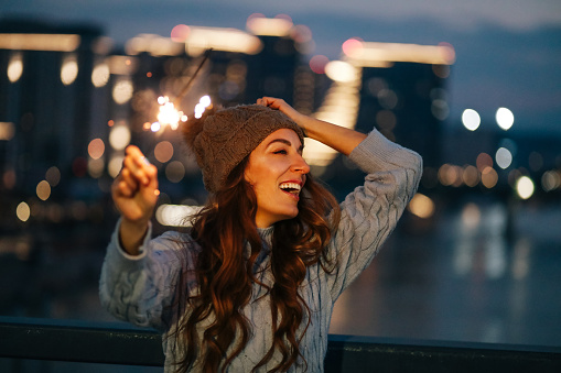 Portrait of a young woman holding a burning sparkle in front of modern city