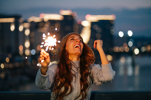 Portrait of a young woman holding a burning sparkle in front of modern city