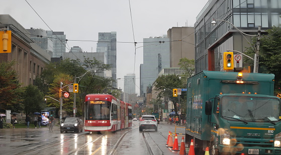 Toronto, Canada - August 23, 2023: Heading east on College Street near Beverley Street. The TTC 506 Carlton streetcar heads west in the Toronto Discovery District by the University of Toronto campus. Rainy morning in summer.