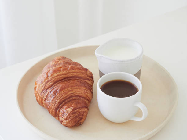 istock Simple breakfast on a tray on the white table. Croissant, coffee cup and milk jug. 1702493516