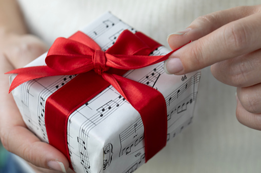 Woman holding gift box. The gift box covered with musical note paper.